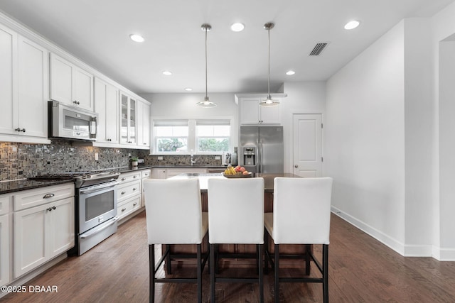 kitchen featuring stainless steel appliances, white cabinetry, a kitchen bar, backsplash, and visible vents