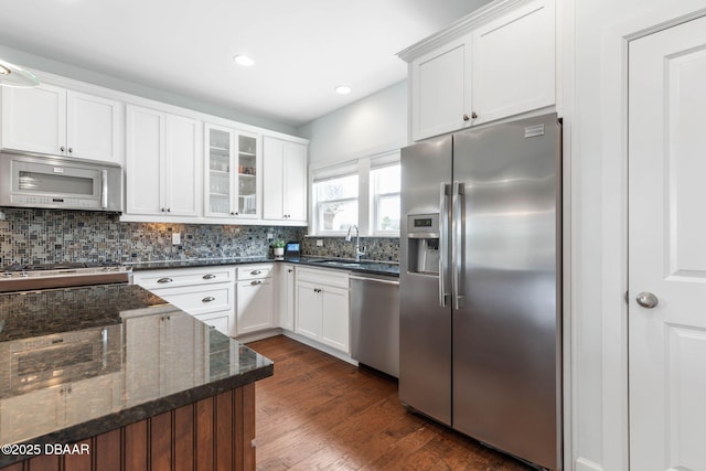 kitchen featuring white cabinets, appliances with stainless steel finishes, a sink, decorative backsplash, and glass insert cabinets