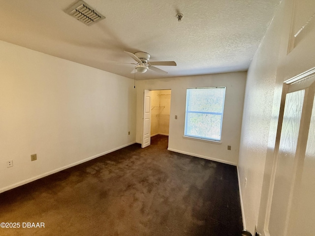 unfurnished bedroom with a walk in closet, dark colored carpet, visible vents, a textured ceiling, and baseboards