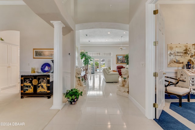 hallway with ornate columns, french doors, ornamental molding, light tile patterned flooring, and a high ceiling