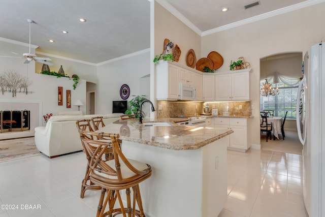 kitchen featuring a kitchen bar, light stone counters, kitchen peninsula, white cabinetry, and white appliances