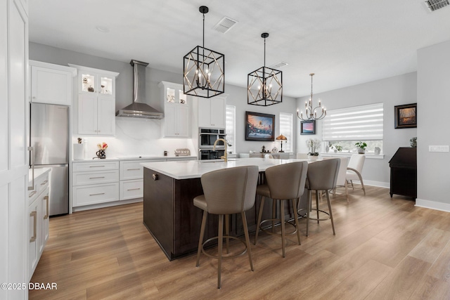 129 Seaside Pt, Flagler Beach, FL 32136 - kitchen with wall chimney range hood, stainless steel appliances, light countertops, a chandelier, and light wood-type flooring