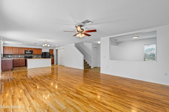 unfurnished living room featuring sink, ceiling fan with notable chandelier, and light wood-type flooring