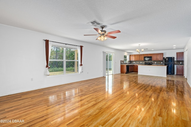 unfurnished living room with ceiling fan with notable chandelier, light hardwood / wood-style floors, and a textured ceiling