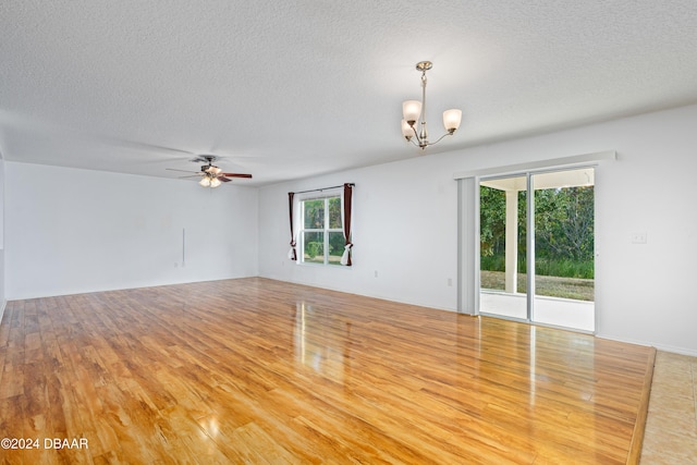 unfurnished room with light wood-type flooring, a textured ceiling, ceiling fan with notable chandelier, and a healthy amount of sunlight