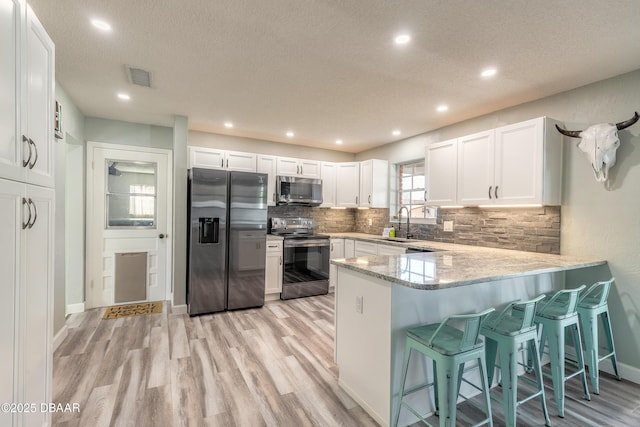 kitchen with sink, tasteful backsplash, appliances with stainless steel finishes, kitchen peninsula, and white cabinets