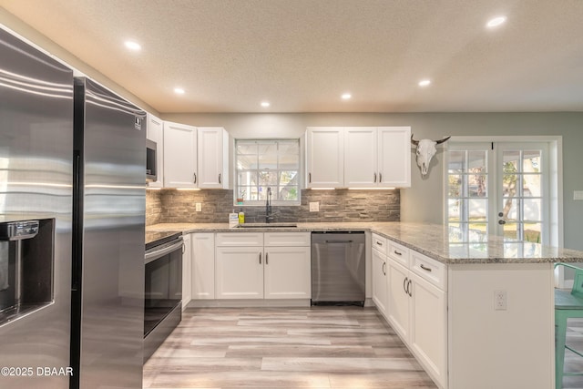 kitchen with sink, white cabinetry, light stone counters, appliances with stainless steel finishes, and kitchen peninsula