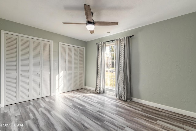 unfurnished bedroom with multiple closets, a textured ceiling, ceiling fan, and light hardwood / wood-style flooring