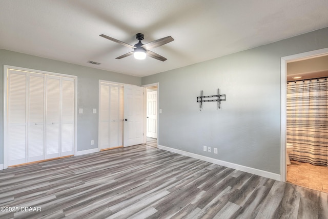 unfurnished bedroom with ceiling fan, ensuite bath, light hardwood / wood-style floors, and multiple closets