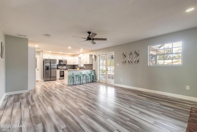 unfurnished living room with ceiling fan, french doors, a healthy amount of sunlight, and light wood-type flooring