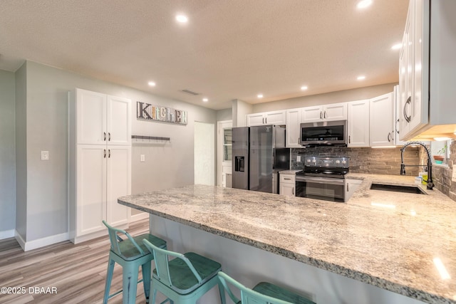 kitchen with a breakfast bar, sink, kitchen peninsula, stainless steel appliances, and light stone countertops