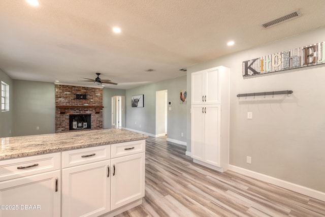 kitchen featuring white cabinetry, a textured ceiling, ceiling fan, light stone countertops, and light hardwood / wood-style floors