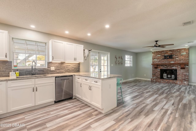 kitchen featuring dishwasher, sink, white cabinets, light stone counters, and kitchen peninsula