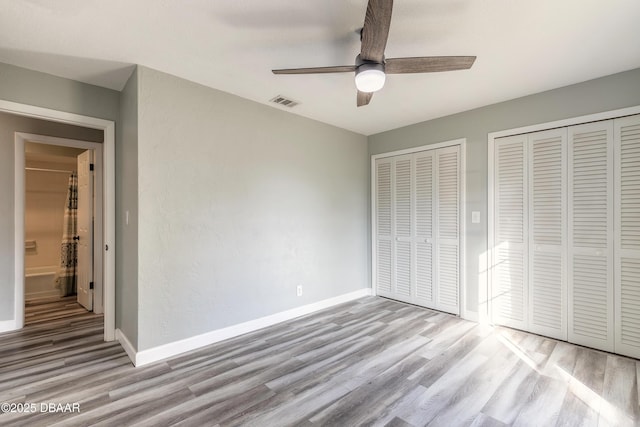 unfurnished bedroom with two closets, ceiling fan, and light hardwood / wood-style flooring