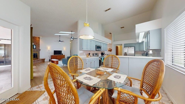 dining area with light hardwood / wood-style floors, sink, ceiling fan, a fireplace, and vaulted ceiling