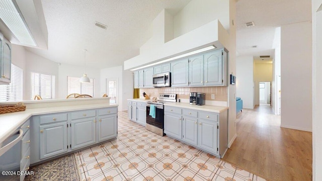 kitchen with appliances with stainless steel finishes, a textured ceiling, pendant lighting, decorative backsplash, and light hardwood / wood-style floors