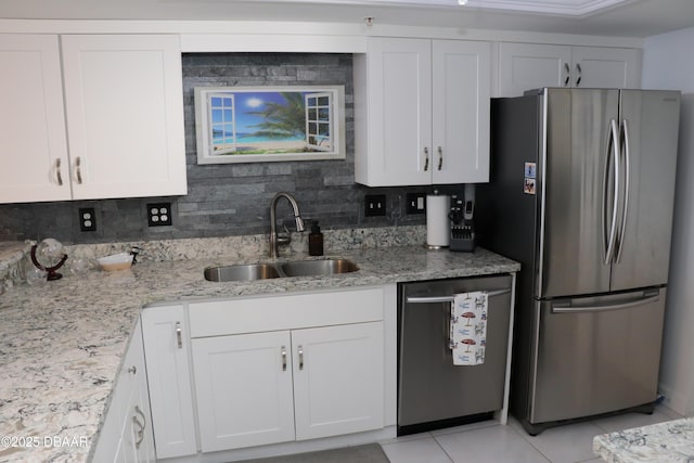 kitchen with light stone counters, appliances with stainless steel finishes, white cabinetry, a sink, and light tile patterned flooring