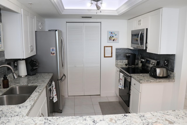 kitchen with a raised ceiling, appliances with stainless steel finishes, white cabinets, a sink, and light stone countertops