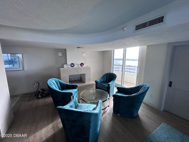 sitting room featuring a textured ceiling, a tiled fireplace, visible vents, and wood finished floors