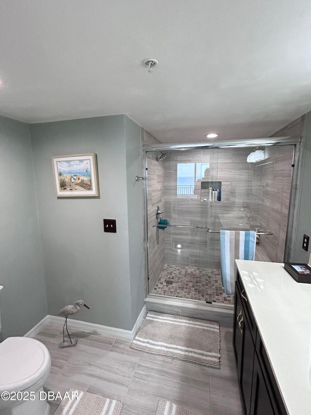 bathroom featuring toilet, a stall shower, baseboards, and vanity