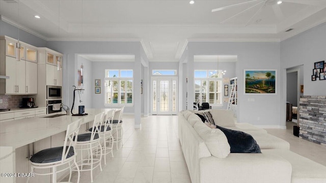 tiled living room featuring a chandelier, a raised ceiling, sink, and crown molding