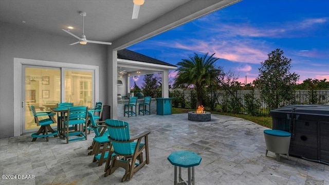 patio terrace at dusk featuring ceiling fan, an outdoor fire pit, and a hot tub