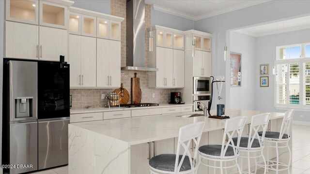 kitchen featuring light stone countertops, white cabinets, wall chimney exhaust hood, and stainless steel appliances