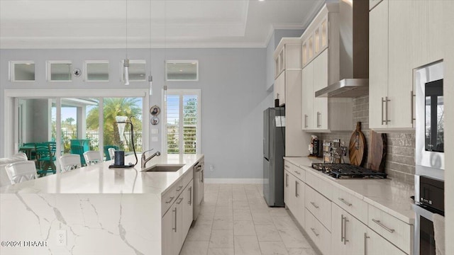 kitchen with stainless steel appliances, sink, light stone counters, wall chimney exhaust hood, and decorative light fixtures