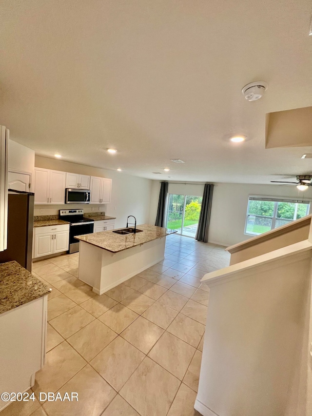 kitchen with stainless steel appliances, a center island with sink, sink, light tile patterned floors, and white cabinets