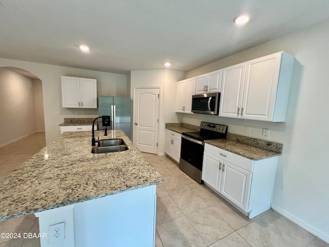 kitchen with a center island with sink, stainless steel appliances, white cabinetry, stone countertops, and sink