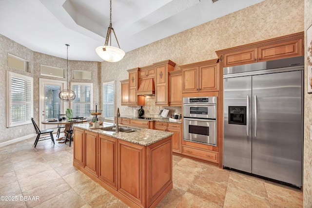 kitchen with light stone counters, brown cabinets, hanging light fixtures, appliances with stainless steel finishes, and a sink