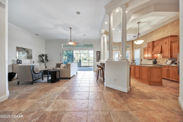 kitchen with brown cabinets, open floor plan, custom exhaust hood, crown molding, and ornate columns