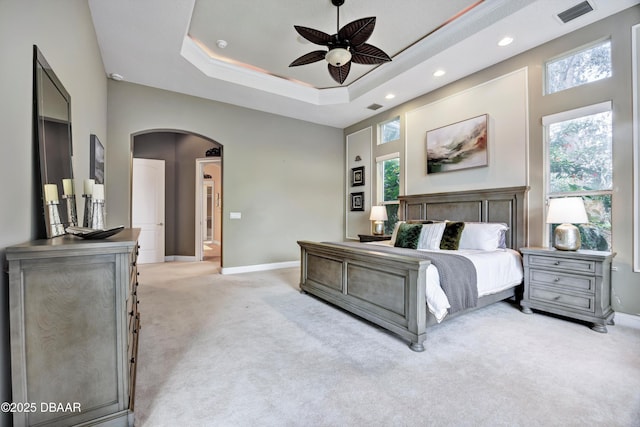 bedroom featuring arched walkways, a tray ceiling, light colored carpet, visible vents, and baseboards