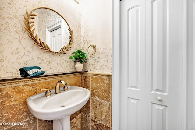 bathroom with a closet, a wainscoted wall, a sink, and wallpapered walls