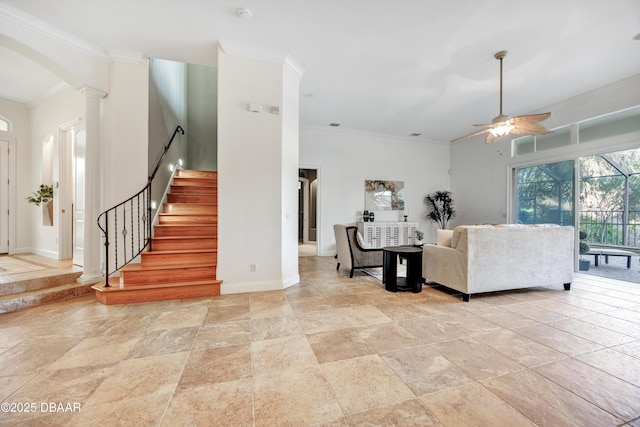 living area featuring arched walkways, decorative columns, ornamental molding, ceiling fan, and baseboards