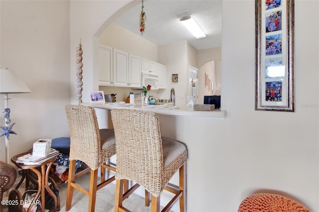 kitchen featuring white microwave, a peninsula, visible vents, white cabinetry, and light countertops