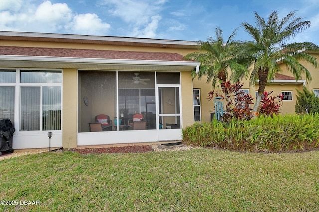 rear view of house with a sunroom, a lawn, and stucco siding