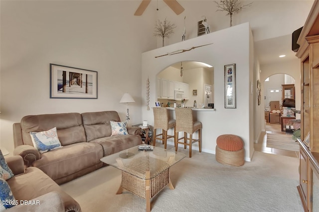 living area featuring light carpet, baseboards, arched walkways, a ceiling fan, and a high ceiling