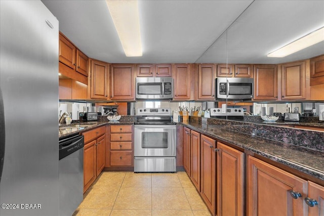 kitchen with stainless steel appliances, sink, dark stone countertops, and light tile patterned floors