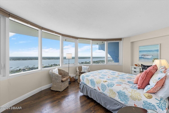 bedroom featuring dark hardwood / wood-style flooring, a water view, and a textured ceiling