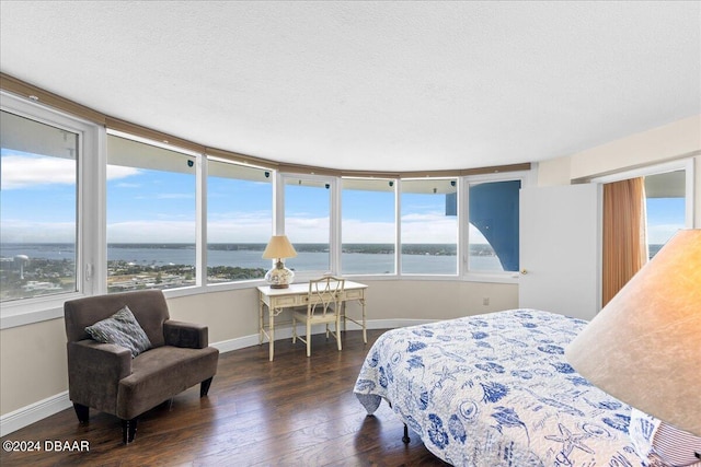 bedroom featuring a textured ceiling, a water view, and dark hardwood / wood-style flooring