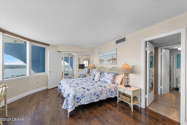 bedroom with ensuite bath, a water view, dark hardwood / wood-style floors, a textured ceiling, and french doors