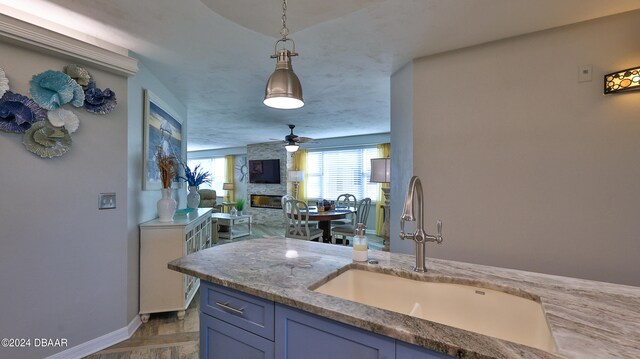 kitchen with a fireplace, ceiling fan, sink, and pendant lighting