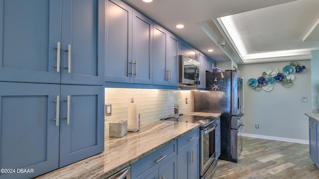 kitchen with hardwood / wood-style flooring, appliances with stainless steel finishes, light stone countertops, blue cabinetry, and decorative backsplash