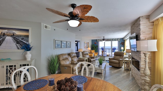 dining area with ceiling fan, light hardwood / wood-style floors, and a stone fireplace