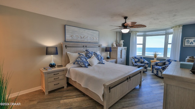 bedroom with ceiling fan, dark hardwood / wood-style floors, and a water view