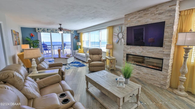 living room with a stone fireplace, wood-type flooring, and ceiling fan