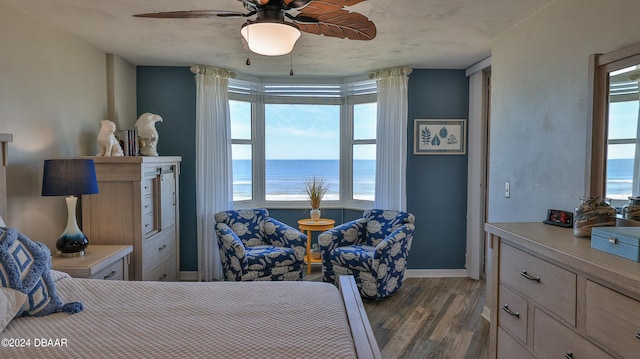 bedroom featuring dark wood-type flooring, a water view, and ceiling fan