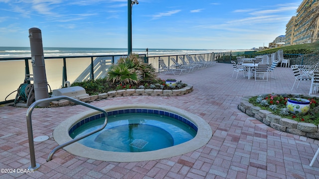 view of swimming pool featuring a hot tub, a patio, a water view, and a beach view