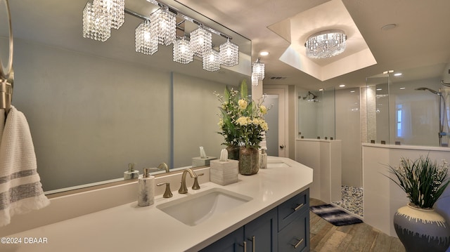 bathroom with hardwood / wood-style floors, a notable chandelier, vanity, a raised ceiling, and walk in shower